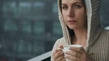 caucasien femme séjours sur balcon pendant chute de neige avec tasse de chaud café ou thé. elle regards à le flocons de neige et respire video