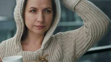 Caucasian woman stays on balcony during snowfall with cup of hot coffee or tea. She looks at the snowflakes and breathes video