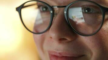 femme dans des lunettes à la recherche sur le moniteur et surfant l'Internet à nuit. le moniteur écran est réfléchi dans le lunettes. travail à nuit. Accueil bureau. éloigné travail video