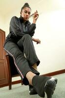 asiático indio mujer vistiendo negro pista traje sentar actitud cadera salto estilo moderno miedoso foto