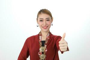 Asian woman traditional red maroon kebaya sharong on white background thumbs up ok focus on face photo