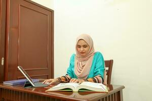 joven asiático malayo musulmán mujer vistiendo Pañuelo a hogar oficina estudiante sentar a mesa computadora libro archivo papel estudiar trabajo foto