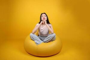 hermosa joven sur este asiático mujer se sienta en un amarillo bolsa de frijoles asiento naranja amarillo color antecedentes actitud Moda estilo elegante belleza estado animico expresión descanso relajarse pensar foto