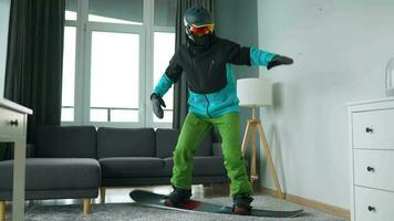 Diversão vídeo. homem vestido Como uma snowboarder passeios uma snowboard em uma tapete dentro uma acolhedor quarto video