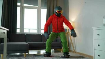 pret video. Mens gekleed net zo een snowboarder ritten een snowboard Aan een tapijt in een knus kamer video