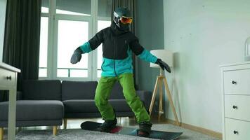 Diversão vídeo. homem vestido Como uma snowboarder passeios uma snowboard em uma tapete dentro uma acolhedor quarto video