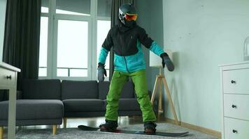 pret video. Mens gekleed net zo een snowboarder ritten een snowboard Aan een tapijt in een knus kamer video