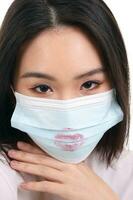 Beautiful young south east Asian woman wearing blue three ply anti virus surgical face mask lipstick lips kiss sign mark on white background look forward photo