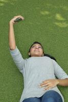 Asian young attractive woman lying on green grass taking selfie self portrait using smartphone photo