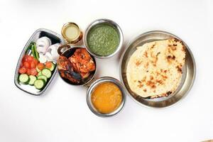 Spicy red Chicken grilled tikka tandoori nan bread green spinach curry yogurt sauce dal tomato cucumber onion salad set in metal stainless steel brass copper pot on white background photo