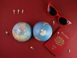 Vaccine passport Malaysia red sunglass world atlas globe map north south pole on red paper background world travel tour vacation mini human figures medical needle syringe bottle photo