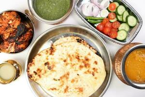 Spicy red Chicken grilled tikka tandoori nan bread green spinach curry yogurt sauce dal tomato cucumber onion salad set in metal stainless steel brass copper pot on white background photo