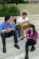 group of Asian young man woman friend student colleagues sting on stairs talk mingle discuss study book note photo