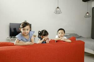 Three little child boy girl brother sister happy smile looking over the sofa photo