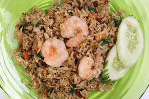 Thai style stair fiend rice with prawn seafood cucumber slice garnish on green glass triangular plate on white background photo