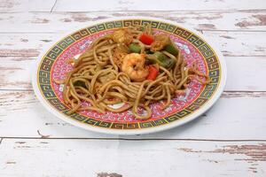 Stair fried noodle with prawn seafood tofu colorful pepper on oriental style plate over rustic wooden background photo