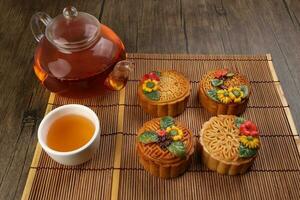 Colorful flower decorated mooncake cut slice half layer Chinese mid autumn festival on bamboo food mat glass teapot white ceramic teacup photo