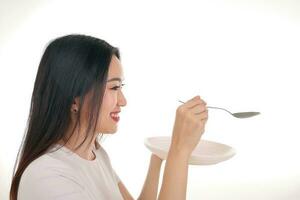 Beautiful young south east Asian woman pretend acting posing holding empty spoon in hand eat taste feed offer white background satisfaction yummy photo