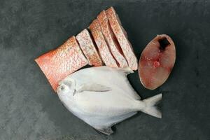 White pomfret Spanish mackerel red snapper fish cleaned descaled degutted sliced fillet pieces on black marble slate background photo