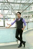 Southeast Asian young office business man wearing vest lean hold on railing stand look at camera confident expression outdoor premises photo