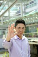Young south east Asian man business office outdoor stand look at camera ok finger sing gesture happy photo