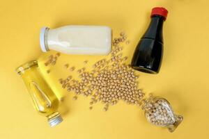 Soyabeans pouring from hart shape glass bottle around bottle of soya bean milk oil sauce on yellow background photo