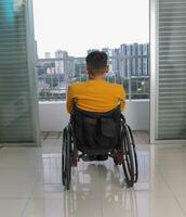 Young man south east Asian malay origin sitting on wheelchair looking outside balcony window. Paralyzed waist down due to accident photo