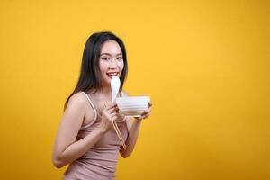 Beautiful young south east Asian woman holding chines empty chopstick Chinese soup spoon bowl utensil pretend acting posing see eat taste smell feed offer satisfaction yummy yellow orange background photo