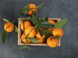 mandarin orange green leaf in wooden box crate top view on black slate marble background photo