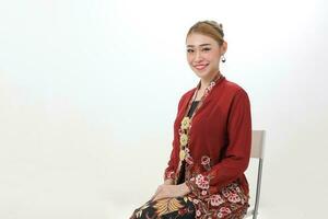 Asian woman traditional red maroon kebaya sharong on white background sitting pose chair sit photo