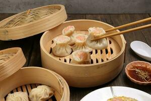 Prawn shrimp shaomai pickup by chopsticks Xiao long bao dim sum dumpling chicken prawn fish seafood vegetable in bamboo steamer fried rice on plate sauce soup spoon over rustic background photo