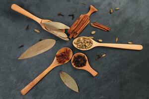 Mix variety spice cinnamon cardamom clove bay leaf wooden spoon scattered on black slate background photo