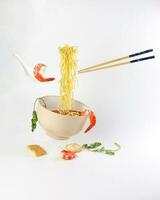 Yellow seafood prawn coriander leaf noodle soup elevated flying suspended in air with soup spoon and chopstick prawn coriander leaf tofu on white background photo