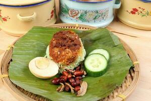 Nasi Lemak fragrant rice cooked in coconut milk served with sambal friend peanut anchovy boiled egg packed in banana leaf on round bamboo plate on wooden background pots containers photo