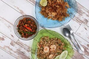 Stair fried flat rice noodles pad thai rice with prawn seafood cucumber slice garnish basil minced chicken spicy on glass color glass plate and bowl fork spoon on rustic wood background photo