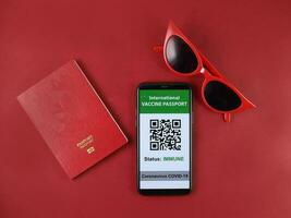 Red eyewear sunglass vaccine passport smartphone book travel vacation red paper background photo