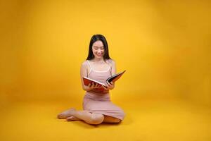 hermosa joven sur este asiático mujer sentar abajo en piso amarillo naranja color antecedentes leer estudiar libro revista actitud Moda estilo elegante belleza estado animico foto