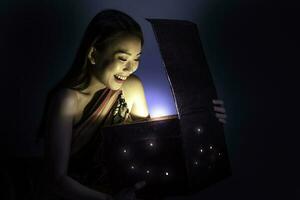 Asian woman opening mystic book box magical light dark background photo