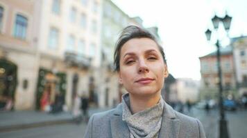 Portrait of a Caucasian woman in a coat in the middle of the old city square. She looking seriously at the camera. video