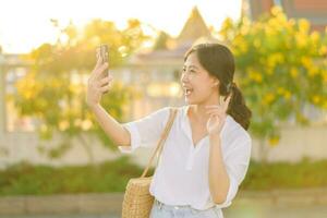 Portrait young beautiful asian woman using smartphone to video call with friend and explore street on summer vacation in Bangkok, Thailand photo