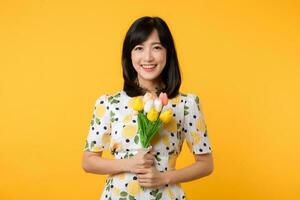 Studio portrait young pretty asian woman happy smile dressing springtime fashion holding tulip bouquet flower against yellow studio background. Person holiday concept. photo