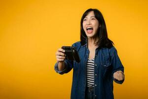 Portrait young asian woman with happy success smile wearing denim clothes holding joystick controller and playing video game. Fun and relax hobby entertainment lifestyle concept. photo