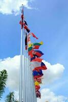 muchas de las banderas de la asean en los coloridos colores soplados por la fuerza del viento ondeando en un poste frente a un hotel en tailandia sobre un fondo con nubes y cielos azules. foto