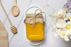 Jar with honey and flowers on wooden background top view, flat lay photo