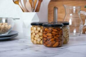 Glass jars with honey and nuts. Almonds, hazelnuts and cashew in honey in kitchen interior photo