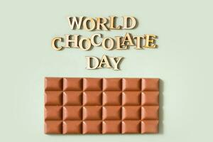 World chocolate day text with chocolate bar flat lay, top view on pastel green background photo