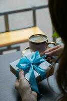 Chocolate craft candy box in female hands with coffee on the table in cafe photo