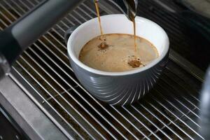 Preparing espresso on professional coffee machine in coffee shop or cafe close up. Pouring strong coffee in grey cup photo