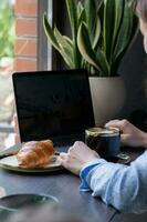 Croissant and female hand with cup of coffee, laptop in cafe. Freelance concept photo
