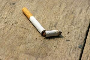 Broken cigarette on a wooden table close up shot. No smoking and ban cigarette concept with a broken cigarette. A broken cigarette on a wooden surface with tobacco powder around it. Burned cigarette. photo